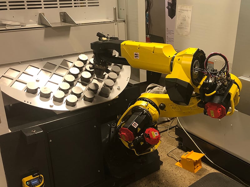 A machine-tending robot adds raw material to the CNC machine and removes a finished product.