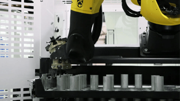 The image depicts a yellow-and-black robotic arm equipped with a gripper interacting with a series of silver cylindrical objects on a machine unit.