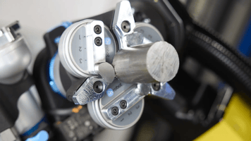 Close-up of an end-of-arm tooling. An electric gripper holding a raw cylindrical part on the end of an industrial robotic arm.