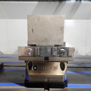 A precision metal base mounted in a machine vise, designed to hold and locate parts in a consistent position. This pallet fixture allows parts to be securely placed, removed, and reinstalled with high accuracy for repeatable CNC machining.
